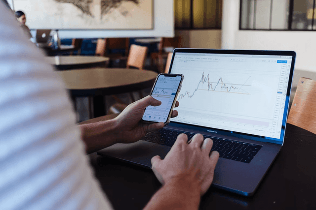 Person using a smartphone and laptop to track the performance of digital assets