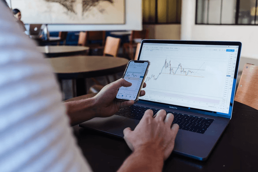 Person using a smartphone and laptop to track the performance of digital assets